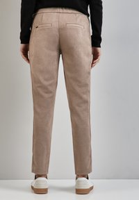 Beiga byxor i mjukt mockaliknande material, med slim fit, två bakfickor och subtila sid sömmar, bärs med vita sneakers.