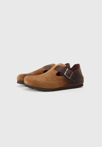 Braune Wildlederschuhe mit einem Ausschnittdesign, ausgestattet mit einem dunklen Lederband und einer Schnallenbefestigung. Strukturiert Oberfläche und Gummisohle.