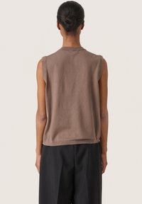Ärmelloses braunes Stricktop mit lässiger Passform, weicher Textur und geripptem Saum. Getragen mit schwarzen weit geschnittenen Hosen, die eine Rückenansicht zeigen.