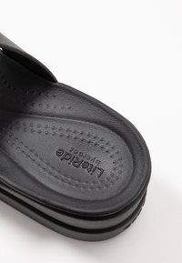 Des sandales noires à enfiler avec une surface texturée, dotées d'une semelle intérieure rembourrée. Le logo de la marque est embossé sur la semelle intérieure.