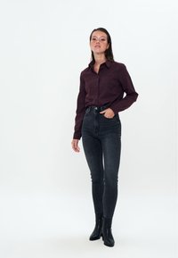 Camicia bordeaux con bottoni abbinata a jeans neri a vita alta e stivaletti. La camicia presenta un colletto e maniche lunghe.