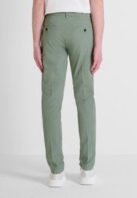 Zelene pamučne hlače slim fit kroja, s jednim pregibom, stražnjim džepovima i kontrastnim crnim gumbima. Uparene s bijelim tenisicama.