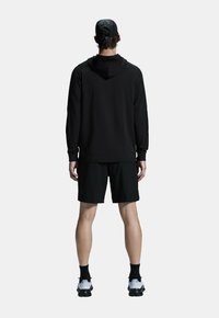 Musta huppari, jossa on huppu, pitkät hihat, yhdistettynä mustiin shortseihin. Henkilöllä on mustat sukat ja valkoiset urheiluvaatteet.