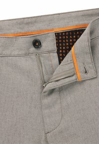 Grå denimbyxor med en svart knapp och orange detaljer. Har en dragkedja i gylfen och ett texturerat inre foder med ett upprepat logomönster.