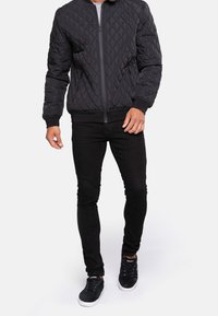 Blouson aviateur matelassé noir avec fermeture éclair, poignets et ourlet côtelés ; porté avec un jean noir slim et des baskets noires.