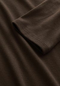Nahaufnahme eines gefalteten braunen Langarmshirts aus Baumwolle, das eine feine Strickstruktur und einen doppelt genähten Saum am Ärmelrand zeigt.