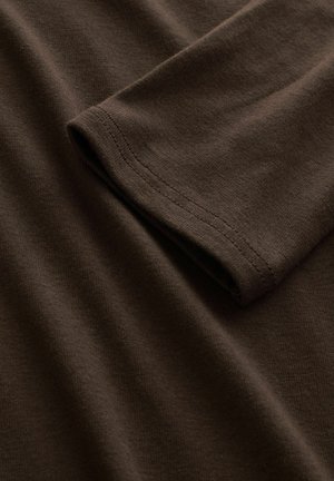 Nahaufnahme eines gefalteten braunen Langarmshirts aus Baumwolle, das eine feine Strickstruktur und einen doppelt genähten Saum am Ärmelrand zeigt.