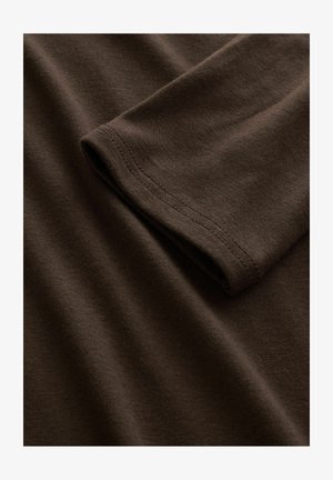 Primo piano di un tessuto di cotone marrone a maniche lunghe piegato, che mostra una fine trama a maglia e un orlo doppio cucito sul bordo delle maniche.