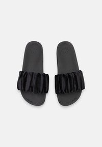 Black slide sandals made of soft velvet with a ruffled strap; flat sole with textured surface. Simple, open-toed design.