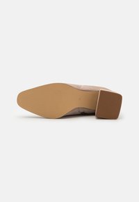 Scarpa con tacco in suede beige caratterizzata da punte quadrate e suola in gomma con un motivo testurizzato. Il tacco è di forma blocco e alto circa 3 cm.