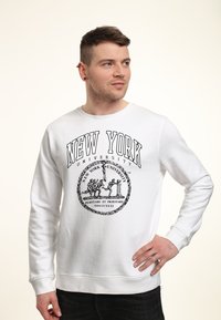 Weißer Sweatshirt mit dem Schriftzug "NEW YORK UNIVERSITY" in fettem schwarzen Text. Das Design enthält ein kreisförmiges Logo mit Figuren und einem Lorbeerkranz.