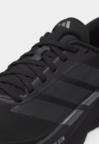 Κοντινό πλάνο μαύρου αθλητικού παπουτσιού με υφασμένες πλευρικές ρίγες, μαύρα κορδόνια και μαλακή σόλα με την επιγραφή "bounce glow".