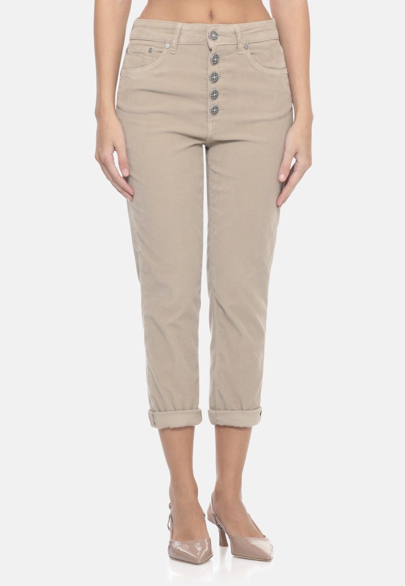 Donna che indossa pantaloni cropped a vita alta beige con quattro bottoni frontali e risvolti, abbinati a décolleté beige a punta.