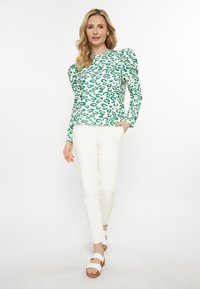 Top a maniche lunghe verde e bianco con stampa leopardata e spalle a palloncino, abbinato a pantaloni bianchi slim-fit e sandali bianchi con suola in legno.
