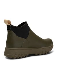 Bottines vert olive avec un panneau élastique noir, semelles en caoutchouc avec des crampons profonds et une languette crème contrastante au talon.