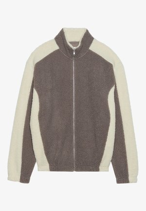Veste zippée marron et crème avec col montant, en matériau pelucheux. Présente un design bicolore et des coutures contrastées.