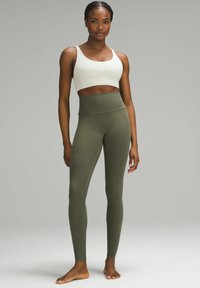 Weißer Sport-BH und olivgrüne High-Waist-Leggings. Beide bestehen aus dehnbarem Material und verfügen über eine glatte Textur sowie ein figurbetontes Design.