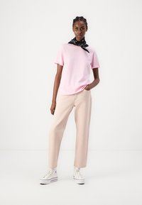 Camiseta de algodón rosa claro combinada con pantalones de denim sueltos color beige. El modelo lleva una bufanda negra estampada y zapatillas altas blancas.