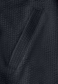 Tissu noir texturé présentant un motif en gaufre subtil avec une poche plaquée étroite. La surface semble douce et légèrement relevée.