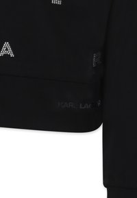 Sweatshirt noir avec des embellissements en strass et un logo imprimé. Le tissu a une texture lisse avec un design court.