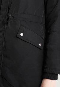 Černá zateplená bunda s texturovanou tkaninou, kapsou na patentový knoflík, stahovací šňůrkou a žebrovanými manžetami pro zvýšení tepla.