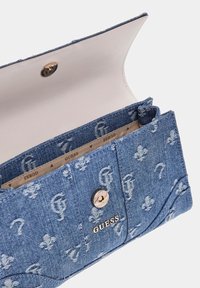 Portafoglio in denim con motivi floreali e chiusura a bottone metallico. Interno beige con il marchio 'GUESS'. Forma rettangolare, bordi cuciti.