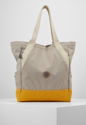Sac fourre-tout en toile beige et jaune avec deux anses beiges, des poches latérales, un patch logo rond et un petit porte-clés sur la lanière gauche.