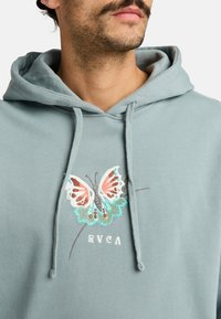 Light blue hoodie made from soft fabric featuring an embroidered colorful butterfly design and the text "RVCA" below.