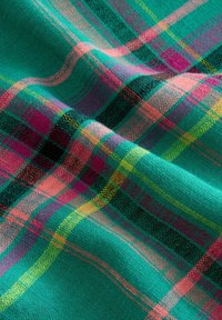 Tissu turquoise avec des rayures à carreaux roses, violettes, jaunes et noires, montrant une texture tissée et de doux plis.