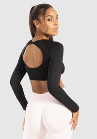 Zwart langwerpig crop top met een ronde uitsnede aan de achterkant, gecombineerd met lichtroze hoge taille legging. Zachte textuur, aansluitend ontwerp.