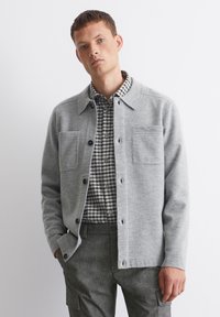 Gray wool cardigan with a collared neck, button front, and two chest pockets, layered over a black and white checked shirt.