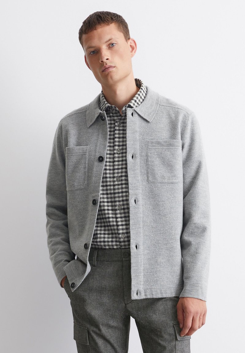 Gray wool cardigan with a collared neck, button front, and two chest pockets, layered over a black and white checked shirt.
