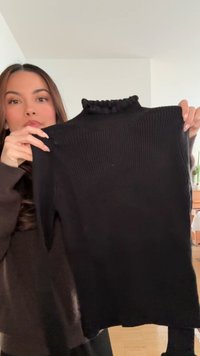 Black ribbed turtleneck sweater with a ruffled neck detail. Features long sleeves and a fitted design, made of a soft fabric.