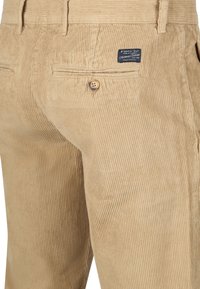 Beige corduroy broek met een achterzak met knoop en een zwart etiket met de tekst "Steppin' Out Authentic Casuals" nabij de tailleband.