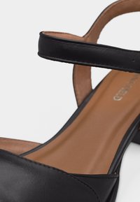 Sandale noire en cuir à bout ouvert avec bride à la cheville et petit talon carré, dotée d'une semelle intérieure beige et d'un design minimaliste.