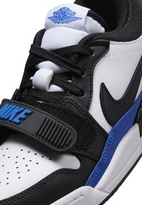 Fekete-fehér sportcipő kék részletekkel, bőr és hálós anyagokból készült, perforált orr, fűzős záródás és állítható szíj "NIKE" márkázással.