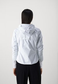 Giacca leggera e impermeabile di colore azzurro, con cappuccio regolabile e polsini elasticizzati. Presenta una tasca sul retro e una silhouette aderente.