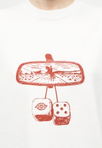 Καθρέφτης οπισθοπορείας που δείχνει έναν καουμπόι να οδηγεί ένα άλογο σε ερημικό δρόμο, με μια θολή ζαριά κρεμασμένη από κάτω που εμφανίζει το λογότυπο της Dickies.