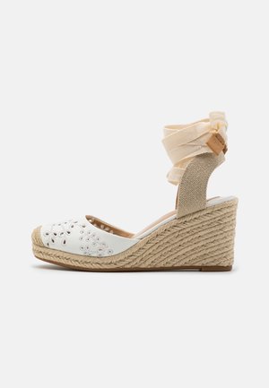 Kileespadrillesandal med beige rebhæl, hvid blomsterudskæring i tåspidsen og kremfarvet stofankelbind med bundet sløjfe.