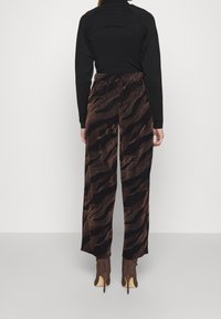 Haut noir à manches longues associé à un pantalon large avec un motif zigzag marron et noir, conçu dans un tissu texturé et brillant.