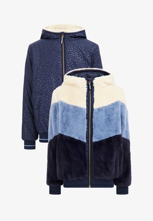 Veste en fausse fourrure bleu marine avec un motif à pois, présentant un design en blocs de couleurs crème et bleu, capuche, fermeture éclair à l'avant et poignets côtelés.