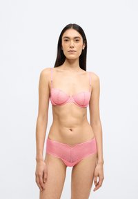 Rózsaszín csipkés fehérnemű szett virágmintával, hullámos szegéllyel a melltartón és az alsón, állítható pántokkal, valamint egy kis dekoratív díszítéssel.