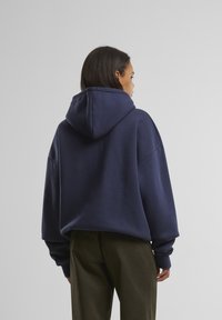 Mørkeblå oversized hættetrøje med en rummelig hætte og nedsatte skuldre, lavet af blødt materiale, med et enkel design og ribbede manchetter.