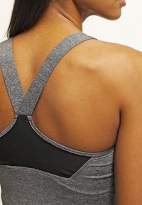 Grå atletisk linne med låg ryggdesign, som har korsade band. Slät textur med detalj i svart nätpanel.