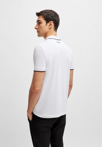 Camiseta polo blanca hecha de algodón, con cuello clásico, mangas cortas y detalles negros en el cuello y los dobladillos de las mangas.