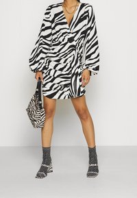 Robe noir et blanc à imprimé zèbre avec des manches bouffantes et un design enroulé ; associée à un sac à imprimé zèbre et des chaussettes grises texturées avec des talons carrés.