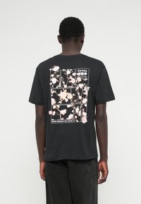 Μαύρο βαμβακερό T-shirt με ανθισμένο γραφικό σε ροζ και λευκό με μπλοκ λεπτομέρειες. Κοντά μανίκια και άνετη εφαρμογή.