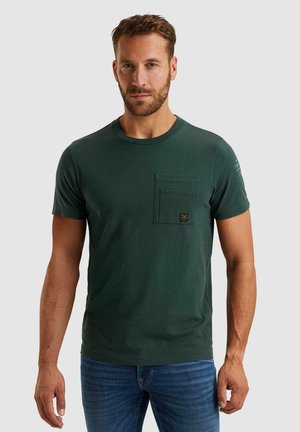 Camiseta de algodón verde con cuello redondo, mangas cortas y un bolsillo frontal que presenta un pequeño parche de logo. Textura suave, ajuste casual.