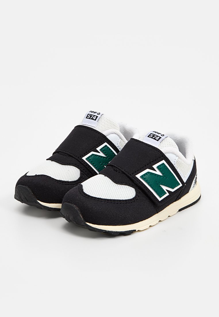 Baskets noir et blanc avec une tige en maille, une sangle Velcro, un logo 'N' vert et une semelle en caoutchouc, avec un intérieur rembourré.