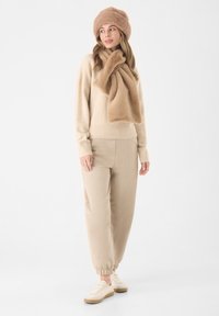 Beige trui en bijpassende joggingbroek, gecombineerd met een zachte beige sjaal en muts. De stof lijkt zacht en heeft een relaxte pasvorm met geribbelde manchetten.